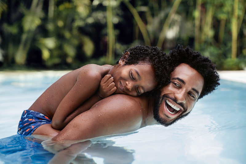 Homem e criança sorriem na piscina